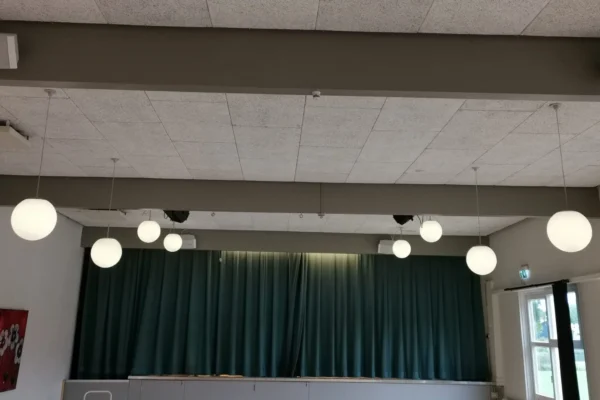 Et hvidt lokale med en scene hvor der hænger et grønt tæppe med 4 højtalere