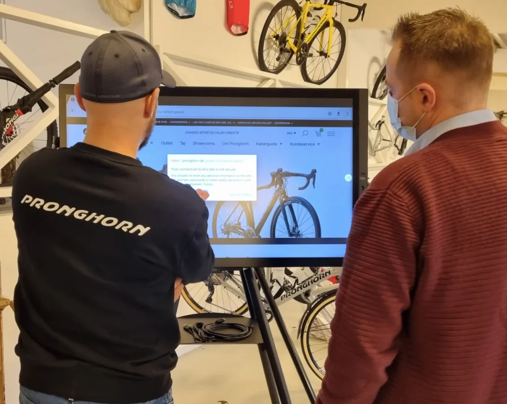 2 mænd i en rød og sort trøje i en cykelbutik har demo af i3 sixty whitborard hos Pronghorn cykler