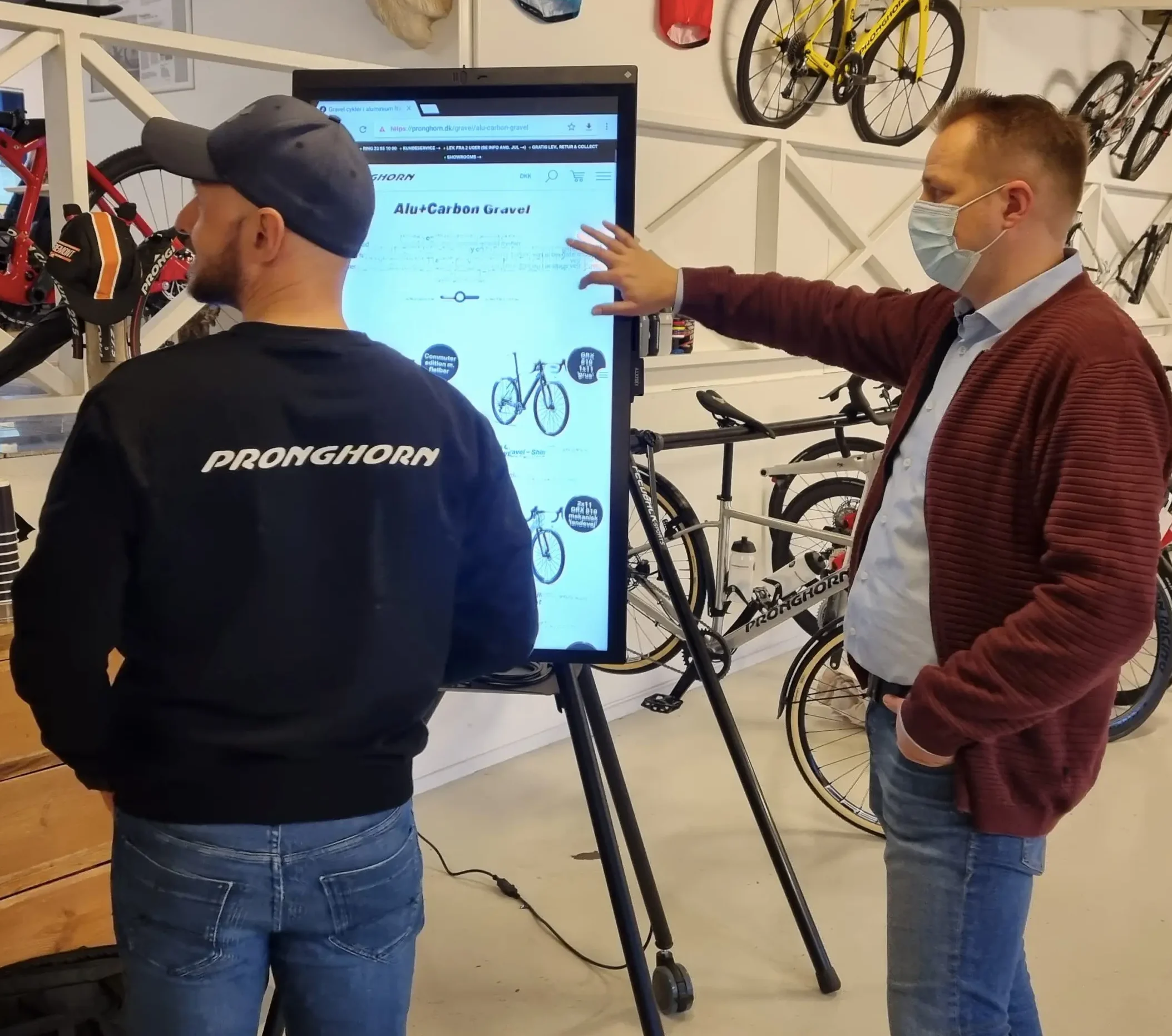 To mænd en i sort og en i en rød trøje står i en cykelbutik for en i3 sixty whiteboard