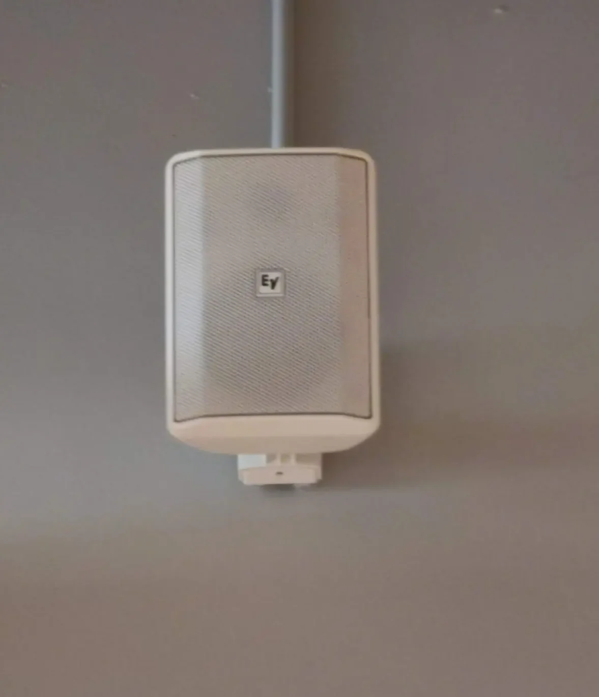 Hvid Voice højtaler monteret på en grå væg i en træningssal